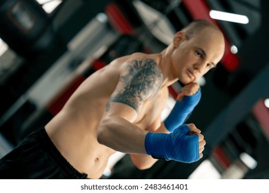 close-up in a boxing fight club bald young boxer with tattoos in blue bandages trains punches shadow boxing professional technique training - Powered by Shutterstock