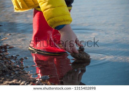 closeup of boy hand playing with pebbles in the lake water wearing rubber boots 