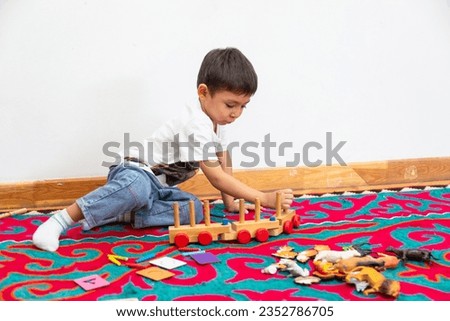 Closeup of boy playing with wooden train toy in kindergarten on a Kyrgyz handmade floor covering Shyrdak