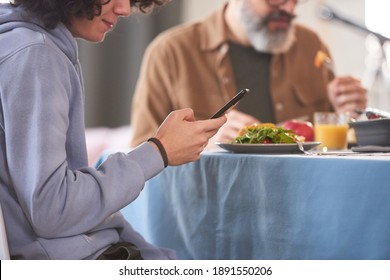 Close-up Of Boy Sitting At Dining Table And Using Mobile Phone During Dinner