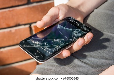 Close-up of a boy's hand looking at his still working phone with a broken screen.