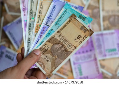 Closeup Of Brand New Colorful Indian Currency Bank Notes Of 10, 50, 100, 200, 500 & Pink 2000 Rupees Bundle Issued And In Circulation After Demonetisation Held With Hand With Many Notes In Background