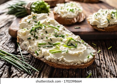 Close-up of bread slice with traditional Slovak bryndza spread made of sheep cheese with freshly cut chives placed on rustic wood.