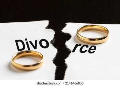 Closeup of a breakup document with the word divorce and two wedding rings on a black table