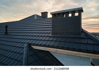 Closeup of brick chimney on house roof top covered with ceramic shingles. Tiled covering of building