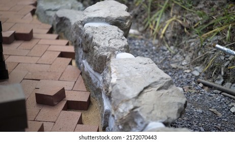 Closeup Of Brick Paver Going Into Place Along A Rock Wall Edge In Hardscaping Landscaping Patio Project.