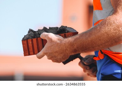 Close-up of Bricklayer constructing brick wall using red bricks, cement and tools while wearing gloves
