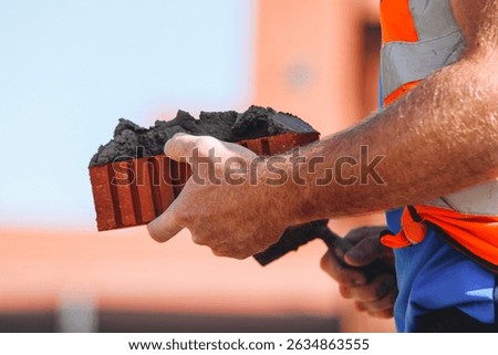 Close-up of Bricklayer constructing brick wall using red bricks, cement and tools while wearing gloves