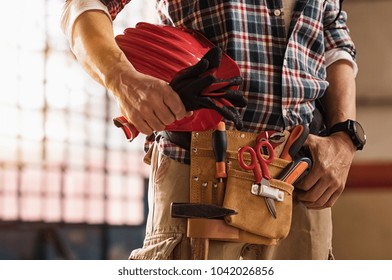 Closeup of bricklayer hands holding hardhat and construction equipment. Detail of mason man hands holding work gloves and wearing tool kit on waist. Handyman with tools belt and artisan equipment. - Shutterstock ID 1042026856