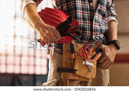 Closeup of bricklayer hands holding hardhat and construction equipment. Detail of mason man hands holding work gloves and wearing tool kit on waist. Handyman with tools belt and artisan equipment.