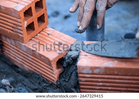 A close-up of a bricklayer's hands using a trowel and mortar to build a red brick wall. Concept of construction, manual labor, skilled craftsmanship, and the building industry.

