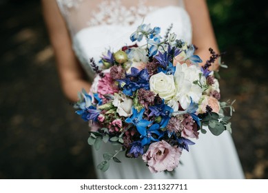 A close-up of bride holding an elegant wedding bouquet, featuring blue and white flowers arranged in a beautiful display