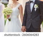 Close-up of a bride holding a white rose bouquet and the groom s hand during their wedding ceremony, highlighting the elegant wedding dress and groom s suit with a boutonniere.