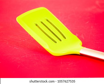 Closeup Of A Bright Neon Green Silicone Spatula Burger Flipper With Stainless Steel Handle Sitting On A Vibrant Red Cutting Board Background.