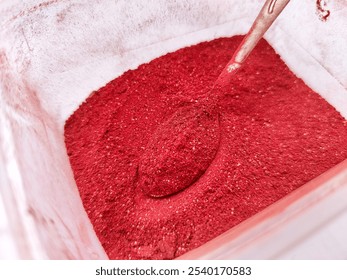 Close-up of bright red powder in a transparent container. A metallic spoon is submerged, highlighting texture and color intensity. Ideal for food, art, or industrial concepts. - Powered by Shutterstock