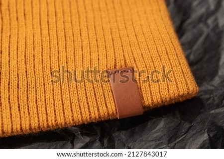 Close-up of a bright woolen knitted yellow hat, male or female. Mockup, brown, leather blank tag sewn on headwear for a logo or brand. Teen uniform or brand