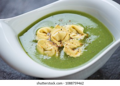 Closeup of broccoli cream-soup with tortellini served in a white bowl, selective focus