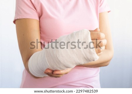 Close-up of a broken arm of a woman in a cast in a pink t-shirt on a white background. Accident insurance.