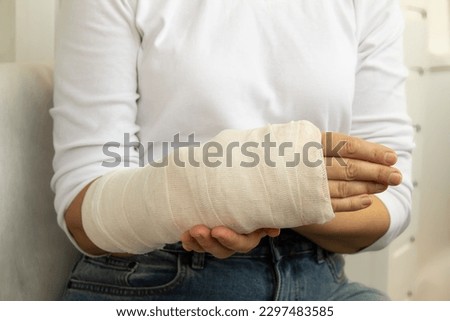 Close-up of a broken arm of a woman in a cast in a white t-shirt on a white background. Insurance medicine concept.