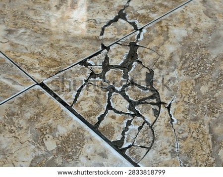 Close-up of a broken brown marble-pattern ceramic tile floor with severe cracks and shattered pieces.