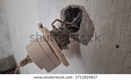 Close-up of a broken electrical socket pulled out from a rough wall, exposing dangerous tangled wiring and a deep hole, symbolizing danger, repair, construction, or electrical failure.