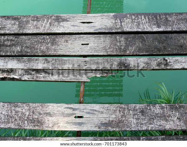 Closeup broken planks of a Wood pedestrian\
suspension bridge with reflection in water canal. Broken wooden\
bridge with missing\
planks.