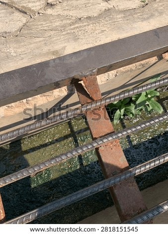 Close-up of a broken welded joint on a rusty metal drainage grate over a mossy concrete ditch.
Damaged and cracked rusted steel frame of a sewer grid cover showing corrosion and need of repair.
High angle view of an old weathered iron drainage grate with a broken bars structure and wild plant in a gutter.