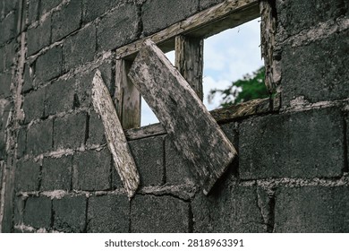 Close-up of a broken window frame with weathered wooden boards on a rough concrete block wall of an abandoned building.