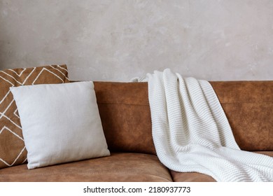 Closeup of brown eco leather couch with soft cushions and knitted white blanket near wall in room indoor. Modern design of living room, dry cleaning furniture concepts - Shutterstock ID 2180937773