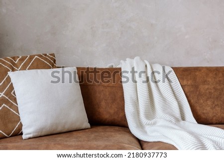 Closeup of brown eco leather couch with soft cushions and knitted white blanket near wall in room indoor. Modern design of living room, dry cleaning furniture concepts