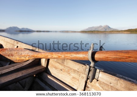 Closeup of brown wooden oar in rowing boat rowlock at sea in sunlight. 