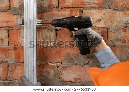 Close-up of a builder assembling metal drywall profiles using electric drill indoor.