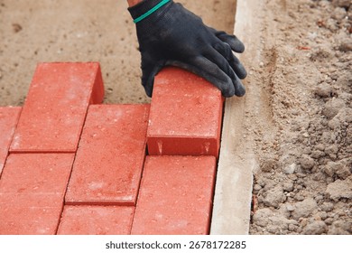 Close-up of builder fitting red paving bricks into  pattern on sandy base