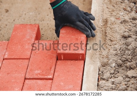 Close-up of builder fitting red paving bricks into  pattern on sandy base
