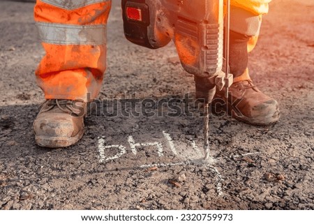 Close-up of a builder using a cordless hammer drill to drill holes in the road at the location marked by the site engineer surveyor