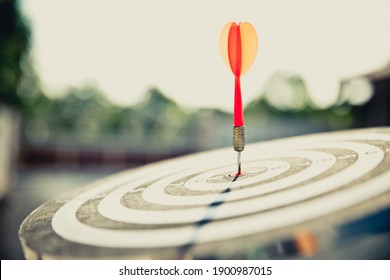 Close-up the bullseye target or dart board has red dart arrow throw hitting the center of a shooting with the sun shines and shadows for business targeting and winning goals business concepts