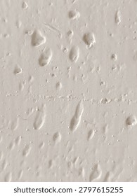 Close-up of bumpy white paint texture with air bubbles and imperfections on a wall surface.