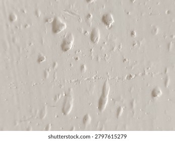 Close-up of bumpy white paint texture with air bubbles and imperfections on a wall surface.