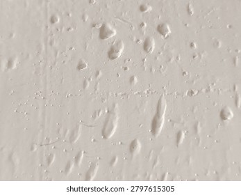 Close-up of bumpy white paint texture with air bubbles and imperfections on a wall surface.