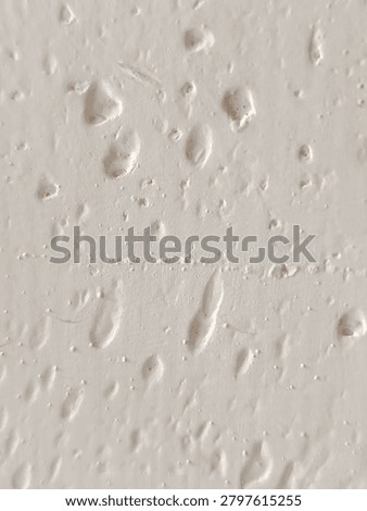 Close-up of bumpy white paint texture with air bubbles and imperfections on a wall surface.