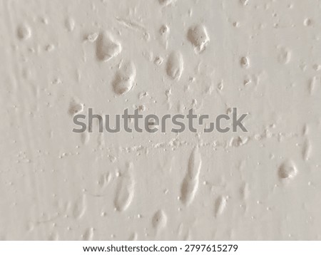 Close-up of bumpy white paint texture with air bubbles and imperfections on a wall surface.