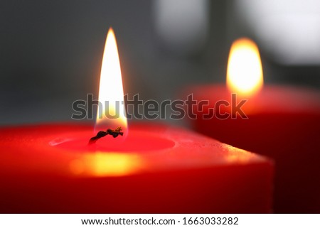 Close-up of burning candle. Red plug light in darkness with focus on single glim in foreground. Background or illustration of memories or celebration. Romantic and cosiness concept
