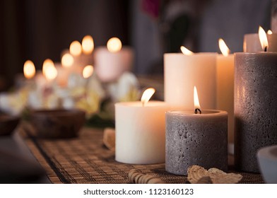 Closeup of burning candles spreading aroma on table in a spa room. Beautiful composition with grey and white candles for spa treatment. Zen and relax concept.