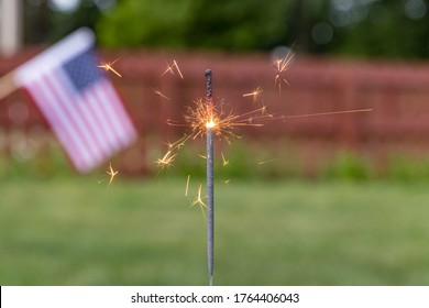 Closeup Of Burning Sparkler And American Flag In Backyard. Concept Of Fireworks Safety, Independence Day And Fourth Of July Celebration