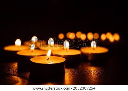 Close-up of burning tea candles in the dark. Reflection of candlelight flame.
