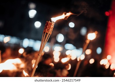 Close-up of a burning torch against a background of blurred lights, creating a bokeh effect. The flame dances gracefully, illuminating the night with a soft, warm glow - Powered by Shutterstock