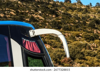 Close-up of bus side mirror with reflection in glass, red curtain and blue roof against rocky mountainside background. Concept of transport, travel, tourism, road trip and scenic journey in nature.