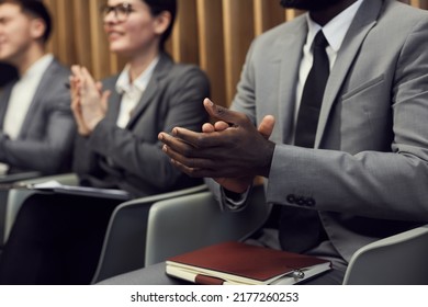 Close-up Of Business Audience Welcoming Conference Speaker: Black Businessman With Diary On Knees Clapping Hands