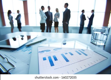 Close-up of business document in touchpad lying on the desk, office workers interacting in the background
