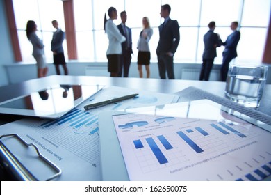 Close-up of business document in touchpad lying on the desk, office workers interacting in the background - Powered by Shutterstock